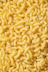 Heap of raw uncooked italian pasta coquillettes over brown texture background. Flat lay. Food background. Macro, close up