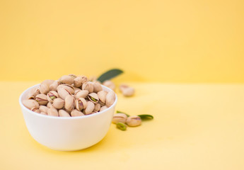 Salted pistachios in a bowl on a yellow background