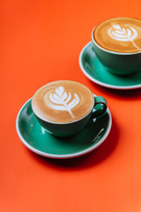 Cyan cappuccino coffee cups over orange background. Top view flat lay with copy space