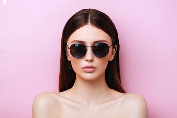 Portrait of an attractive young girl in round glasses on a pink background in studio