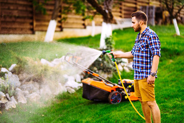 Close up of smiling man watering backyard lawn using hose. Irrigation systems.