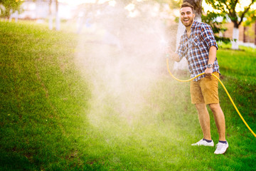 Gardening details and maintainance- man playing with hose and watering the lawn