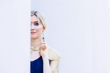 Close -up portrait of european blond girl in asian or indian dress with nice earrings on white background. Woman with bright make up half face is hidden.