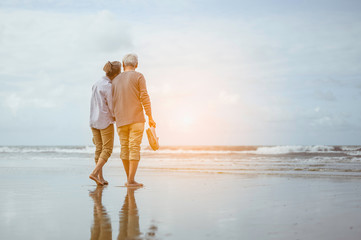 Senior couple walking on the beach holding hands at sunset, plan life insurance at retirement concept.