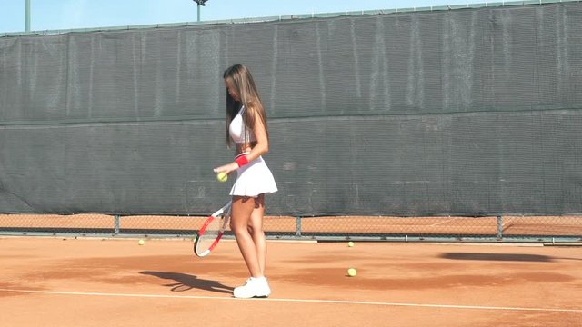 Girl tennis player training on the court with a racket and a ball.