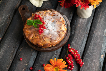 homemade apple pie on a dark brown wooden backdrop decorated with mint leaf and red current