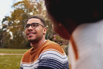 Close-up of a smiling young african man wearing eyeglasses sitting with her girlfriend at park