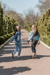 Obraz premium Two smiling young female girl friends having fun in park. Two teen student young woman in jeans