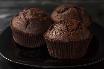 Three chocolate muffins on a black plate on a dark background close up