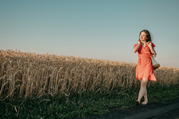 Happy young woman in red dress with bread and loafs in net grocery bag on wheat field sun background. eco friendly, zero waste, slow life concept