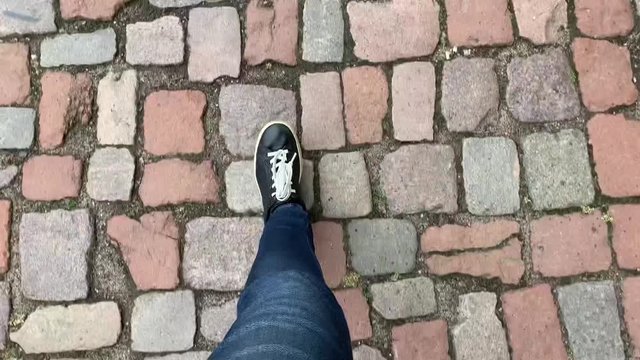 Feet in black sneakers walking over city stepping over sett road