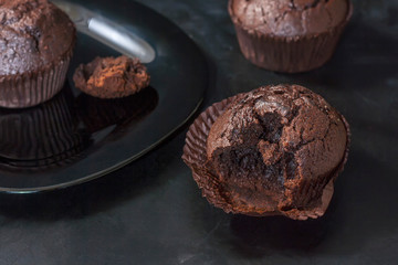 Bitten chocolate muffin on a black background on a dark background close-up.