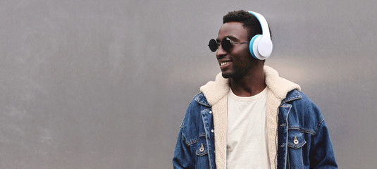 Portrait happy smiling african man in wireless headphones listening to music looking away at blank copy space gray metal wall background