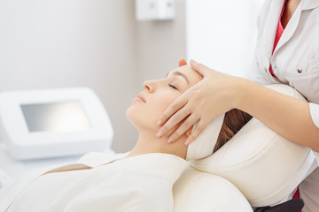 Unknown masseuse beautician doing a face massage to her client a beautiful young woman. Skin care concept