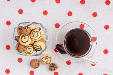 A vase with cookies and a cup of coffee. A glass cup stands on a saucer. Near a teaspoon.