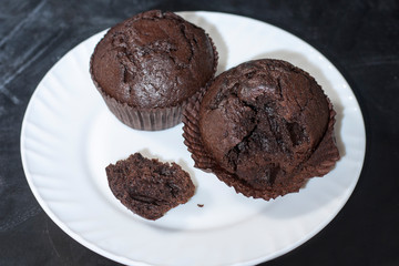 Chocolate muffins on a white plate on a dark background.Close up
