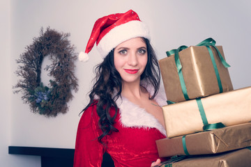 Curious young Santa girl, Christmas hat holding box with gift present on grey wall background. Happy New Year celebration holiday party concept.
