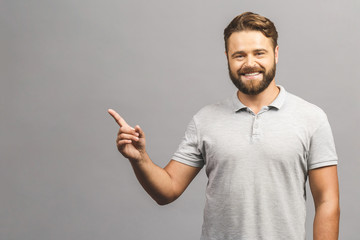 Look over there! Happy young handsome man in jeans shirt pointing away and smiling while standing against white background