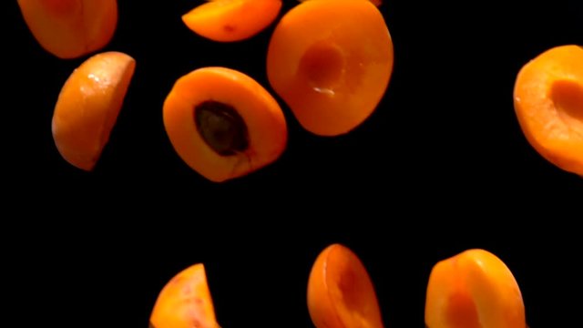 Halves ripe apricots fly on a black background closeup in slow motion