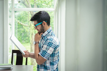 Fototapeta premium Young beard caucasian holding and reading book or notebook, expressing a happy moment.