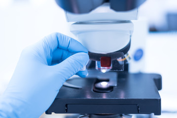 Selective focus technician hand holding microscope glass slide for scientist diagnosis and blurry microscope lens at cytology and pathology department in the hospital.