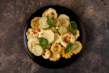 Fried zucchini served with fresh basil leaves. Seasonal organic vegetable meal on a dark concrete background. Healthy cooking. Flat lay, close up.