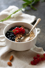 Tasty and healthy organic breakfast. Oatmeal with blueberries and red currants, nuts and chia seeds in a white bowl. Dietary nutrition, health care. Still life with food and flowers. Selective focus.