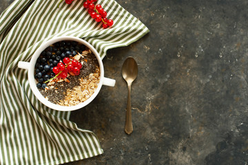 Nice oatmeal bowl on striped kitchen napkin. Oatmeal with blueberries and red currants, chopped nuts and chia seeds in a white bowl. Dietary nutrition. Selective focus, copy space, flat lay.