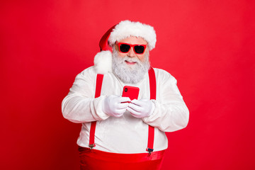 Fototapeta na wymiar Portrait of funny funky fat overweight santa claus with big abdomen belly use cell phone comment newyear posts wearing stylish trendy eyewear eyeglasses hat reading news isolated over red background