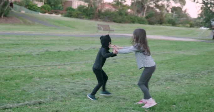 A little boy wearing a black homemade ninja mask for Halloween chases a girl around a park, they wrestle for a moment then she runs away with him chasing her