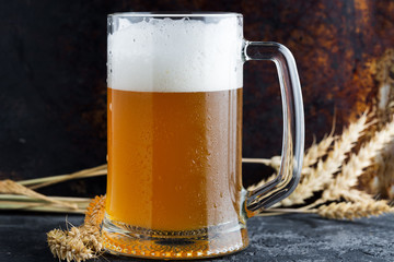 Mug of wheat beer on a rusty dark background with ears of wheat