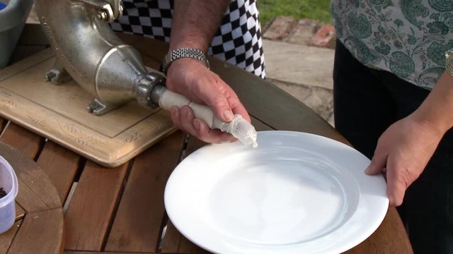 Handheld, medium close up shot of person stuff pork into a stuffer machine and casing it onto a plate.