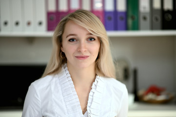 Portrait of a pretty manager blonde girl at work in a white blouse in the office at the table. Right in front of the camera in various poses.