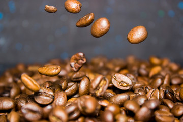 Roasted coffee beans pour from above, hovering in the air on a dark background. Side view, close-up