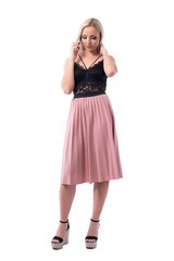 Relaxed young pretty woman in skirt and top talking on the phone looking down. Full body isolated on white background.