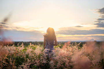 Trendy girl in stylish summer dress feeling free in the field with flowers in sunshine.