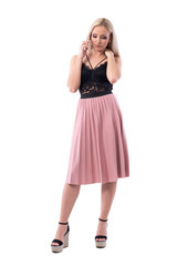 Serious worried pretty blond hair woman talking on the cellphone looking down. Full body isolated on white background.