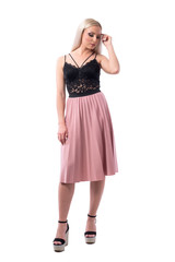 Blonde fashion woman in salmon skirt and platform sandals touching hair looking down. Full body isolated on white background.