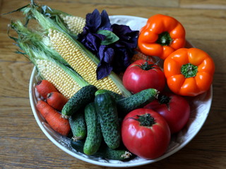 Assorted vegetable, including tomatos, cucumbers, sweet peppers, carrots, corn and basil on a large round white plate