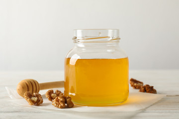 Walnuts, dipper, parchment and glass jar with honey on white background, copy space