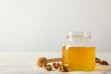 Walnuts, dipper, parchment and glass jar with honey on white background, copy space