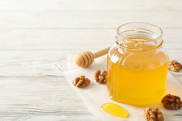 Walnuts, dipper, parchment and glass jar with honey on white background, copy space