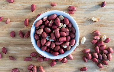 Peanuts nuts in a white bowl located in the middle, peanuts are scattered around the nuts, top view