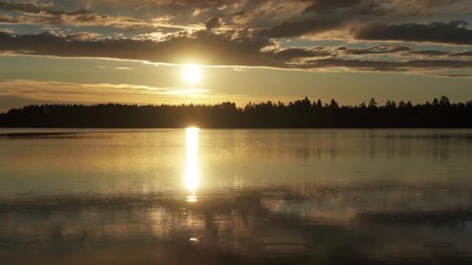 Timelapse of sunrise over calm summer lake and low flying clouds. Sun is reflected in a lake surface like in a mirror