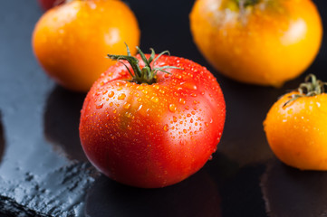 Colorful red and yellow tomatoes on a stone surface wet in drops.