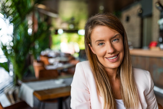 Portrait of a cheerful businesswoman sitting at the table and looking at camera. Stylish attractive young businesswoman with a lovely smile. Single confident smiling woman