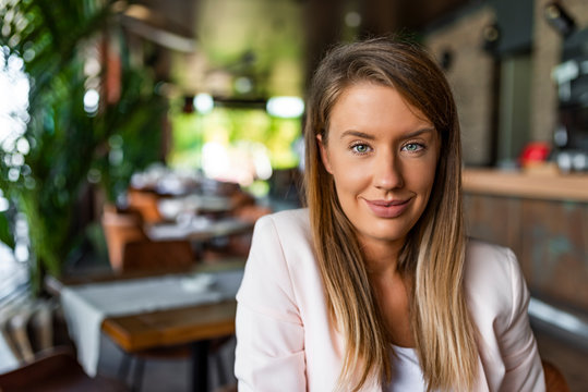 Portrait of a cheerful businesswoman sitting at the table and looking at camera. Stylish attractive young businesswoman with a lovely smile. Single confident smiling woman