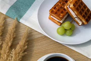 Breakfast. Cup of black coffee with Belgian waffles on wooden background.
