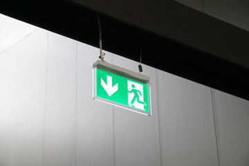 emergency exit or fire escape sign with green running man symbol and directional arrow hanging from...