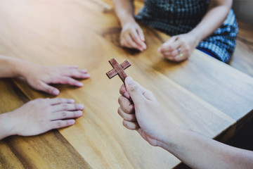 Close up of Young christian man holding small wooden cross in hands while explains about Jesus story and sharing gospel to his unbeliever friends around wood table indoor ,  great commission concept.
